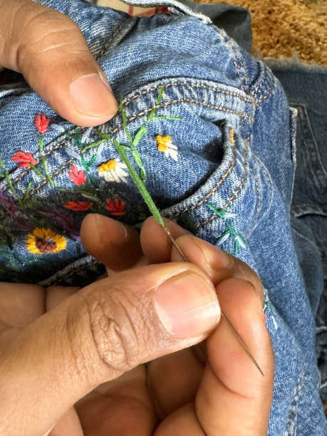 全画幅图片，女裁缝/裁缝用彩色线在蓝色牛仔裤的后口袋上绣上花朵和叶子，雏菊和向日葵从后口袋里长出来，定制牛仔裤，重点在前景图片下载
