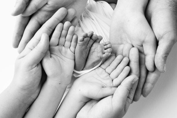 爸爸的手掌，妈妈都抱着刚出生的婴儿的脚。新生儿的脚放在父母的手掌上。工作室微距黑白照片的一个孩子的脚趾，脚跟和脚。图片下载