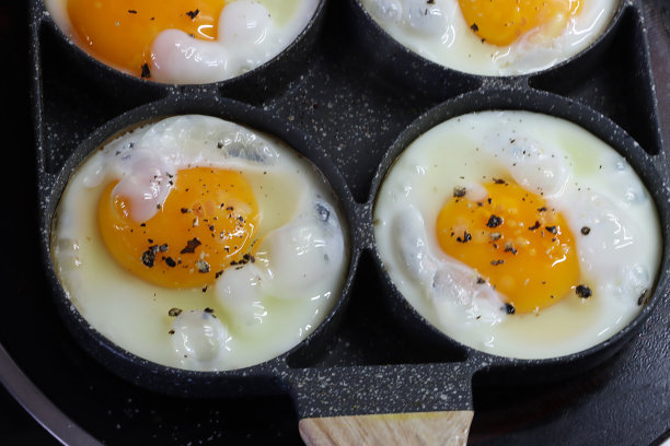 特写图片:带有煎蛋环的不粘锅，四个鸡蛋在陶瓷滚刀上的煎锅里煮图片下载