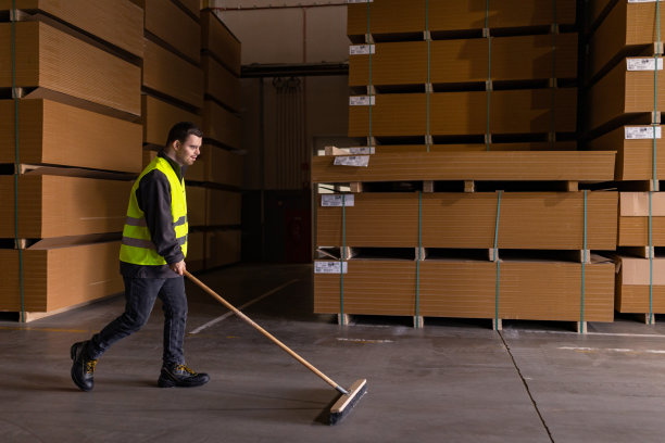 患有唐氏综合症的年轻人在工厂、仓库扫地的照片。残疾工人的概念，在工作场所的支持。图片下载