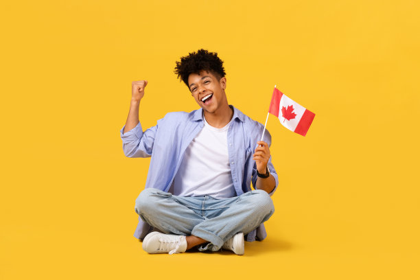 快乐的男学生拿着加拿大国旗在黄色背景上欢呼图片下载
