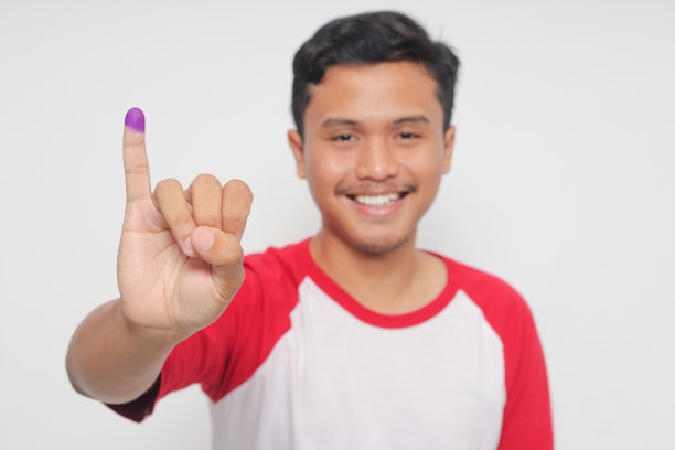 图为一名兴奋的亚洲男子在印度尼西亚总统和政府大选投票后，用紫色墨水蘸着小指的照片。隔离在白色背景上图片下载