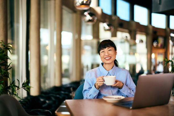 一个微笑的亚洲女人在餐厅工作时端着一杯咖啡的照片。图片下载
