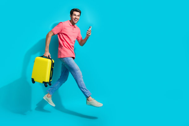 穿着粉色t恤的兴奋男子全身照片，拿着行李高高地跳着叫出租车，空旷的空间孤立的蓝色背景图片下载