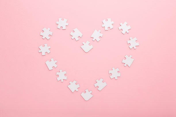 心形由白色拼图片创建在浅粉色的桌子背景。柔和的颜色。特写镜头。爱和关系的概念。自顶向下视图。图片下载