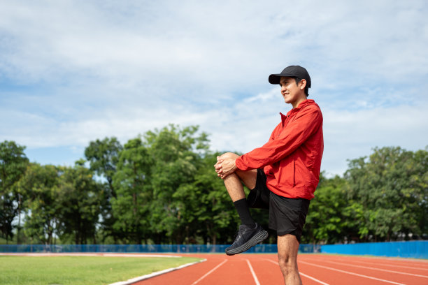 年轻的亚洲男子穿着运动服在户外跑步。印度男子在体育场跑道上跑步前伸展腿的照片。训练运动员在户外运动的概念。图片下载