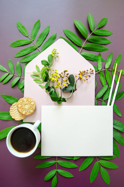 扁平的特写粉红色的模型信封，里面装满了黄色的小花和小叶子，周围是春天的绿叶，白色的卡片模型和一杯咖啡，饼干，暗紫色的背景图片下载
