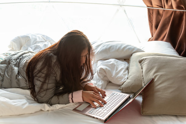 快乐的女人躺在露营帐篷的床上用笔记本电脑工作，远程学习。自由职业者，远程工作，假期工作，节假日，网购教育理念。图片下载