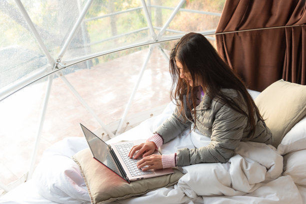快乐的女人在露营帐篷的床上用笔记本电脑打字和工作，远程学习。自由职业者，远程工作，假期工作，节假日，网购教育理念。图片下载