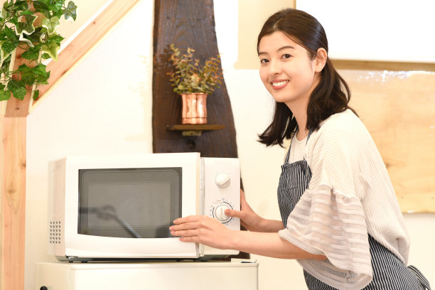 漂亮的年轻亚洲女人在室内用微波炉微笑图片下载