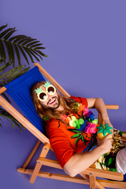 垂直照片乐观的人戴着太阳镜坐在扶手椅上与鸡尾酒在沙滩上的棕榈孤立的紫色背景图片下载