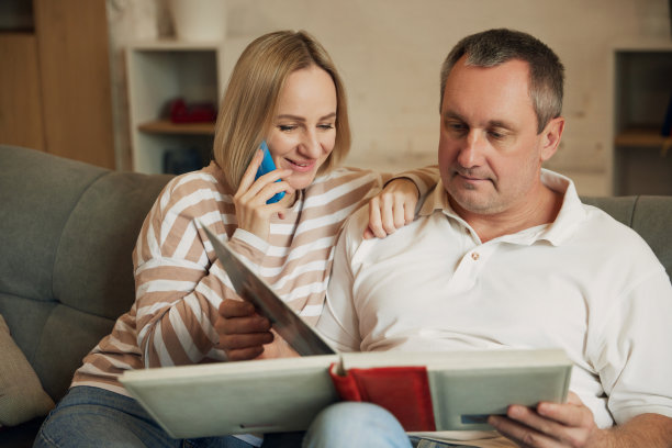 中年夫妇坐在沙发上翻看家庭相册的照片。一个女人微笑着和别人打电话图片下载