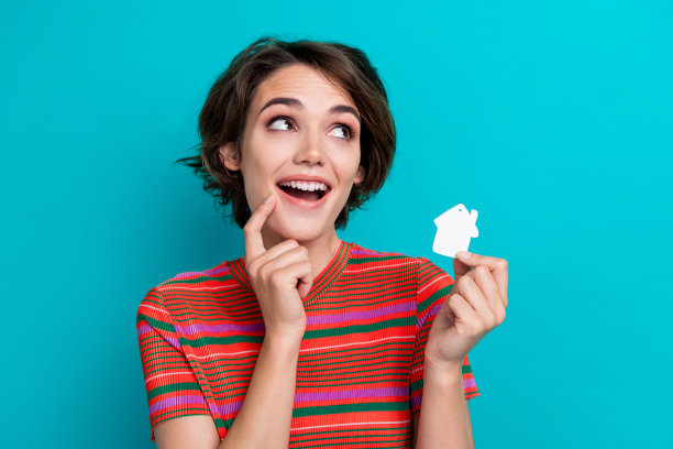 照片中聪明的女人穿着条纹t恤，在蓝绿色的背景上看房子，房地产主张空旷的空间图片下载