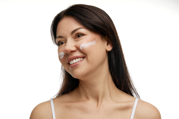 漂亮的中年妇女，穿着奶油色的衣服，在白色的工作室背景下看着别处。皮肤的自我护理和保护。图片下载