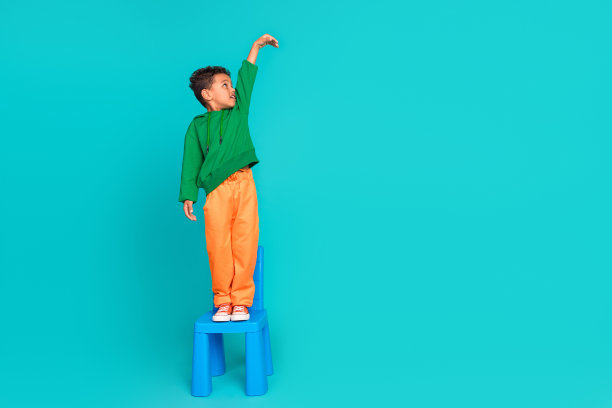 可爱的青春期前男孩站在椅子上的全长照片举起手测量尺寸产品空白空间孤立的青色背景图片下载