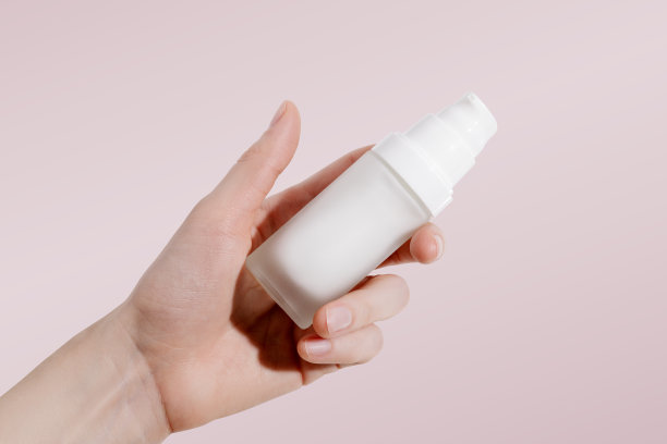 手握空白的白色管粉红色的背景。化妆品美容产品品牌模型。图片下载