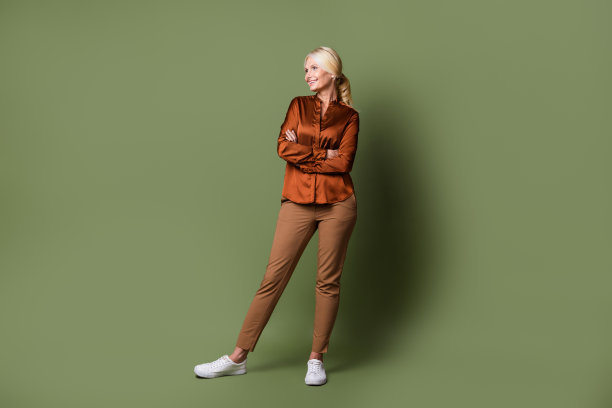 漂亮退休女性的全尺寸照片，双手合十，看起来空无一物，穿着时尚的丝绸棕色衣服，孤立在卡其色背景上图片下载