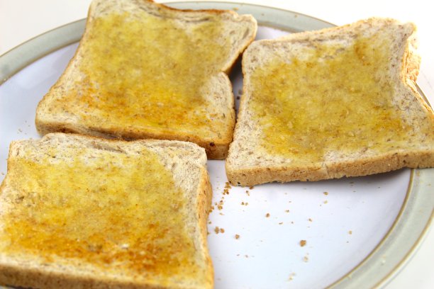 白色盘子里放着三片涂了黄油的吐司图片下载