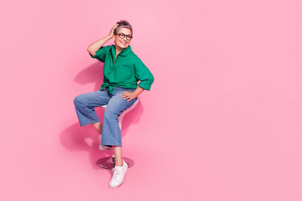 满意的女人全身照片穿着绿色衬衫触摸新发型在美容院坐在凳子上孤立的粉红色背景图片下载