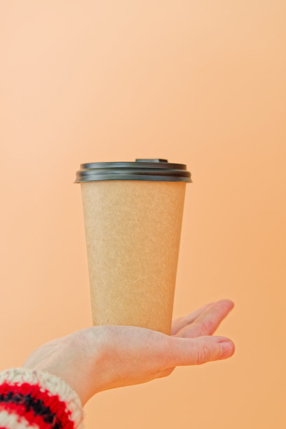 一只手拿着一个纸杯，杯盖上有雪花图案，橙色背景，垂直照片，广告或演示概念图片下载