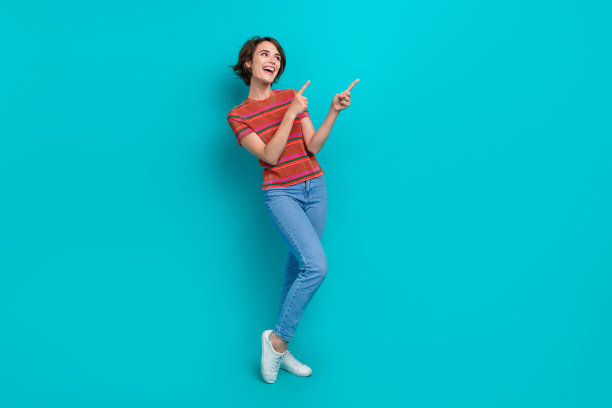 满意的可爱女孩穿着时髦的衣服的全身照片推荐质量的产品，在青色背景上看起来空的空间孤立图片下载