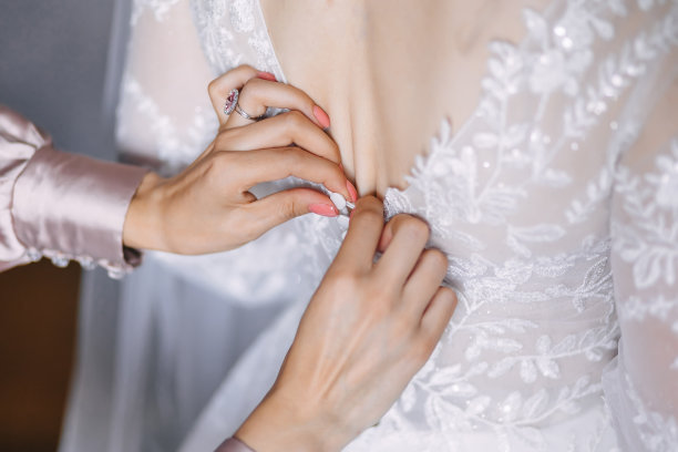 伴娘为新娘的婚礼做准备。这个女孩在婚礼前帮新娘系紧婚纱的束腹图片下载