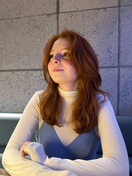 在餐厅背景下拍摄的迷人的年轻女子的特写照片，她长着一头红色波浪状的长发，穿着模拟高领套头衫和意大利吊带裙，微笑着，前臂靠在桌子上，大头照，肖像，聚焦于前景图片下载