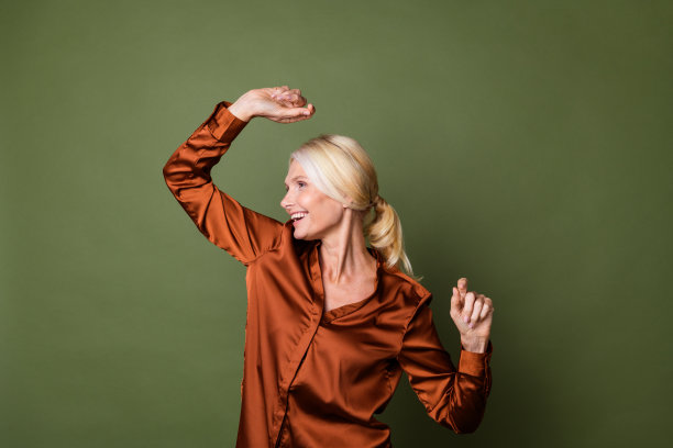 照片中乐观的女人穿着丝绸衬衫，金色的头发，尾巴看起来空空荡荡，在绿色的背景上跳舞图片下载