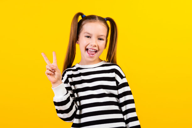 照片中兴奋友好的小孩穿着条纹毛衣微笑着，显示出v字孤立的黄色背景图片下载