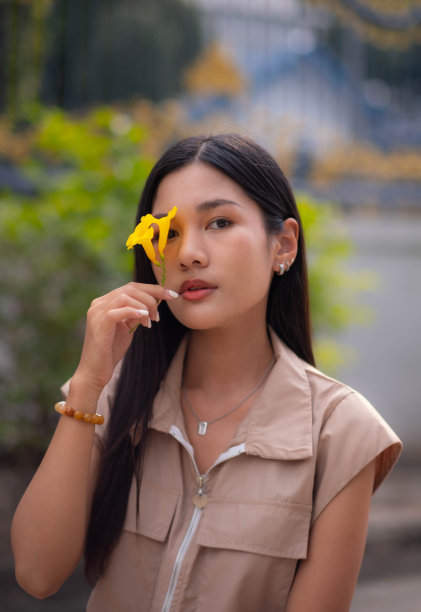 一个十几岁的女孩穿着复古的连衣裙，手里拿着一朵黄色的花，闭上眼睛看着镜头。图片下载