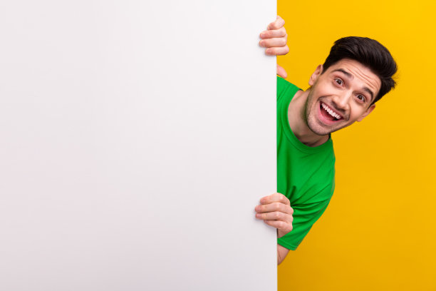 穿着绿色t恤的时髦积极的男人的照片，手表从墙上空出来，在黄色的背景上宣布出售图片下载