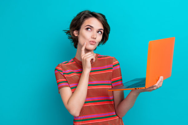 照片中若有所思的女人穿着条纹t恤，拿着笔记本电脑，看起来空空荡荡，选择产品孤立在绿松石色的背景上图片下载