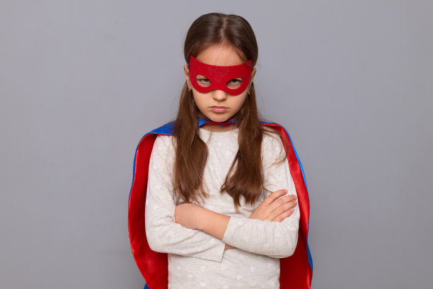 伤心不开心被冒犯的小女孩穿着超级英雄的服装，戴着面具，在灰色的背景中孤立地站着，双臂交叉，表情悲伤图片下载