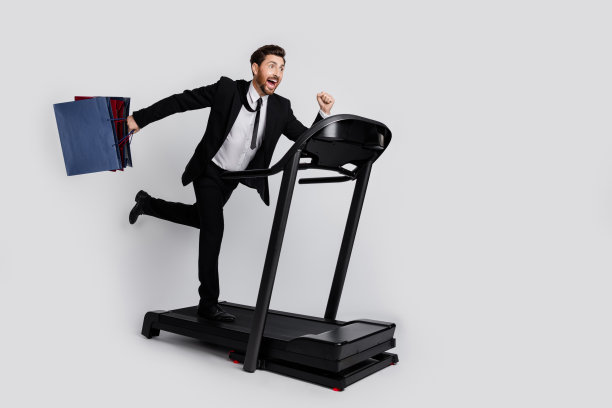 大喜过望的优雅男子手持购物袋跑跑步机空的空间和孤立的灰色背景的全长侧面肖像图片下载