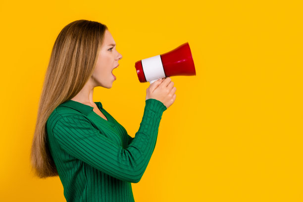 侧面照片，愤怒的棕色头发的年轻少女拿着扩音器与黄色背景的示威者交谈图片下载