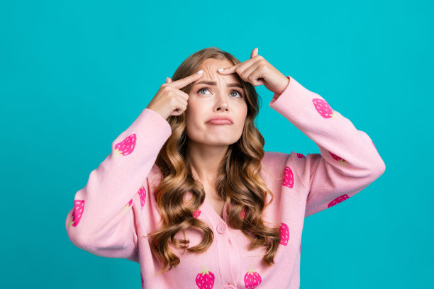 年轻的不快乐的女士的肖像照片，在粉红色的魅力套头衫，她挤压脸皮肤，痘痘额头孤立的蓝色背景图片下载