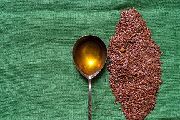 亚麻种子。勺子里装满了亚麻籽油。绿色背景。图片下载