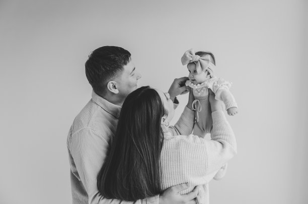 父亲和母亲呕吐女儿特写。幸福的家庭在节日里拥抱可爱的宝宝。爸爸，妈妈牵着婴儿的手。爸爸，妈妈抱着小女孩，头发上扎着蝴蝶结，孤立在墙上。黑白照片。图片下载