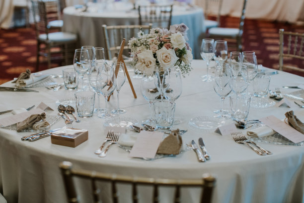 一张为婚宴装饰的桌子的细节照片。白色调装饰:桌布、餐具、透明玻璃、金色椅子、花卉装饰。图片下载
