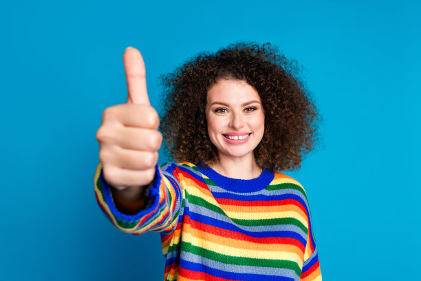 有吸引力的年轻女子的照片肖像大拇指好的质量穿着时尚的彩虹印花衣服孤立的蓝色背景图片下载