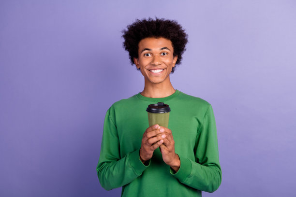 照片中积极开朗的男子穿着绿色毛衣喝咖啡，空旷的空间孤立的紫罗兰色背景图片下载