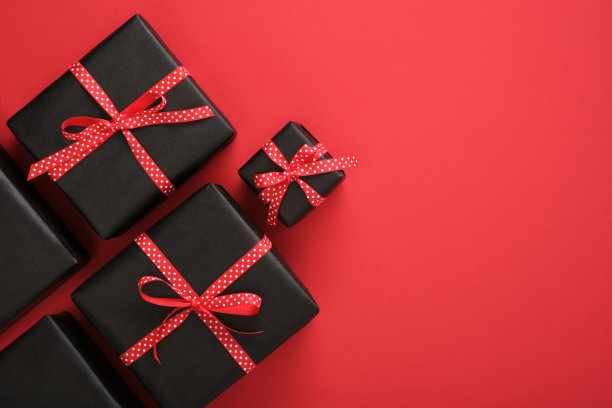 黑色礼品盒，红色背景上点缀着红色缎带。为你的文字留出空间。图片下载