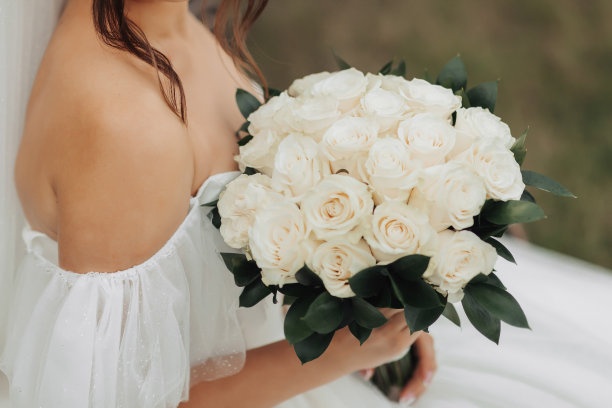 裁剪照片。新娘身穿白色领口礼服，手持一束白玫瑰。漂亮的手和银饰。法国修指甲。新娘的肖像。图片下载