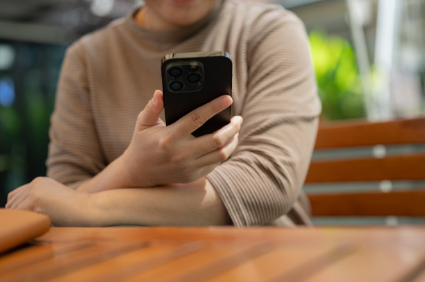 一个女人在户外的桌子上休息时使用智能手机的裁剪照片。图片下载