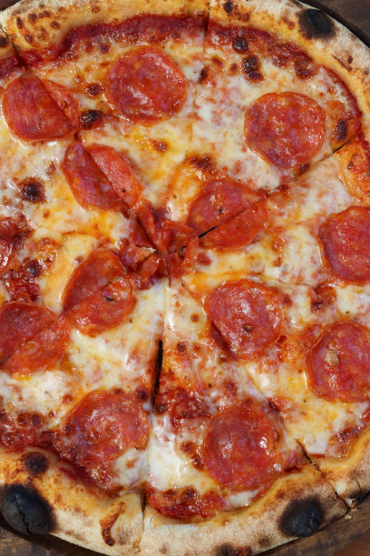特写图片:切片的意大利辣香肠披萨放在木制的披萨板上，融化的金色水牛马苏里拉奶酪和丰富的番茄马里纳拉酱浇头，高架视图图片下载