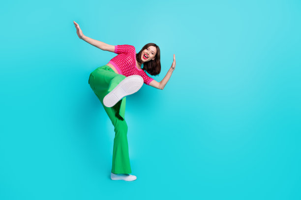 全尺寸照片的好心情疯狂的女孩穿粉红色针织顶绿色裤子显示你的鞋底孤立的蓝色背景图片下载