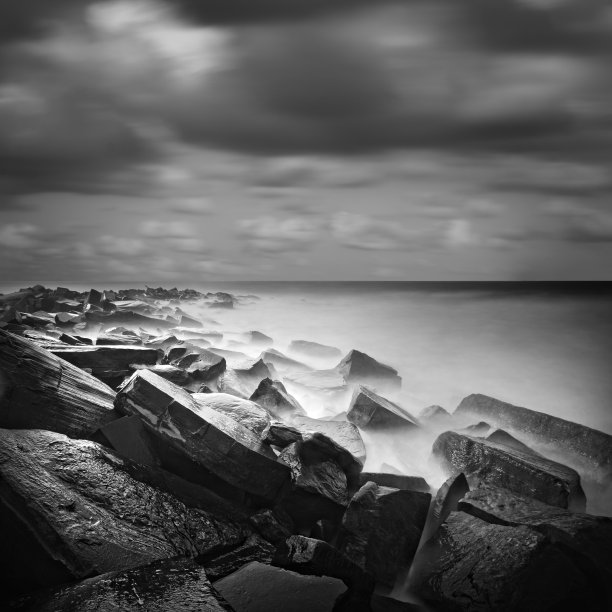 使用长曝光技术拍摄的黑白照片，描绘了淹没在海中的方形岩石。库存图片图片下载