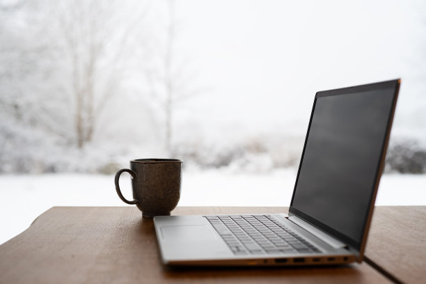 笔记本电脑和一杯咖啡放在木桌上，外面是冬天的风景和雪图片下载
