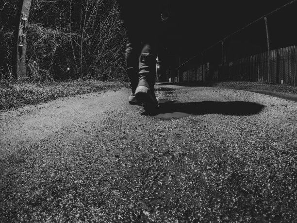 一个女孩在黑暗中走在潮湿的冬日路上回家，从下到上看黑白照片，脚踩在路上图片下载