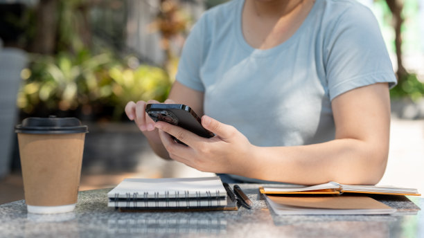 一名亚洲女性坐在咖啡馆的户外餐桌上使用智能手机的裁剪照片。图片下载